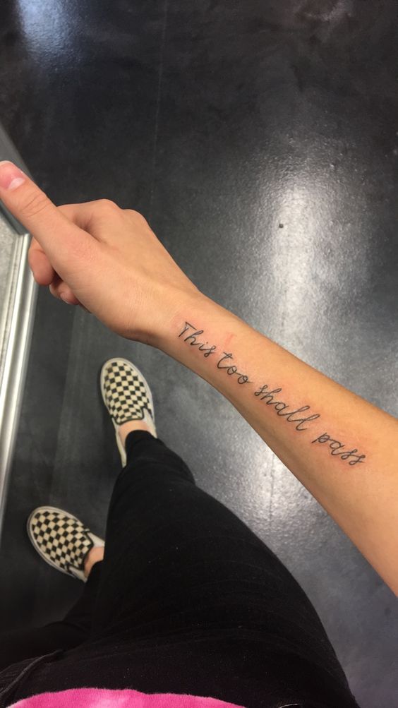 "This too shall pass" tattoo in cursive on the forearm.