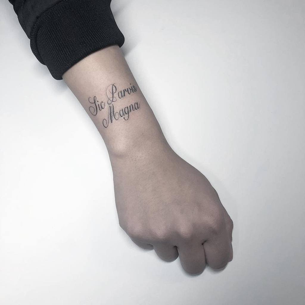 Tattoo on inner forearm reading "Sic Parvis Magna" in elegant script