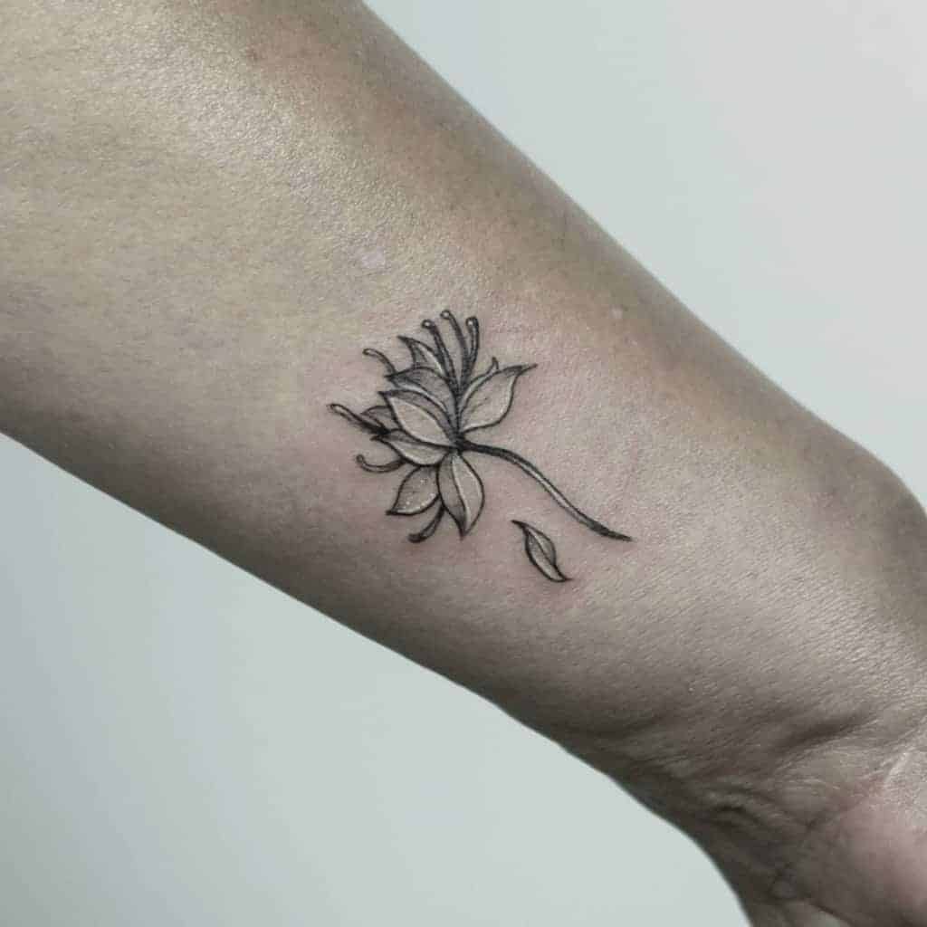 Black ink lotus tattoo on forearm with a small detached petal below
