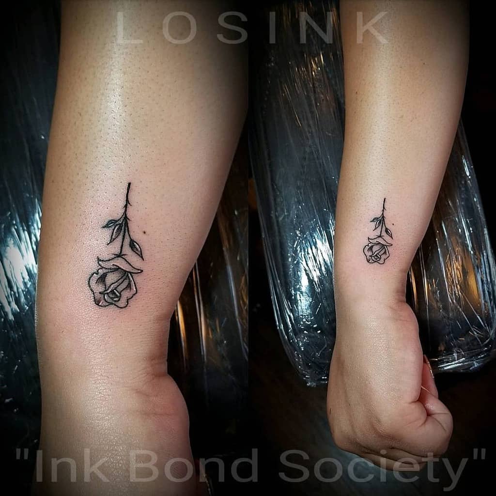 A minimalist black rose tattoo on a forearm