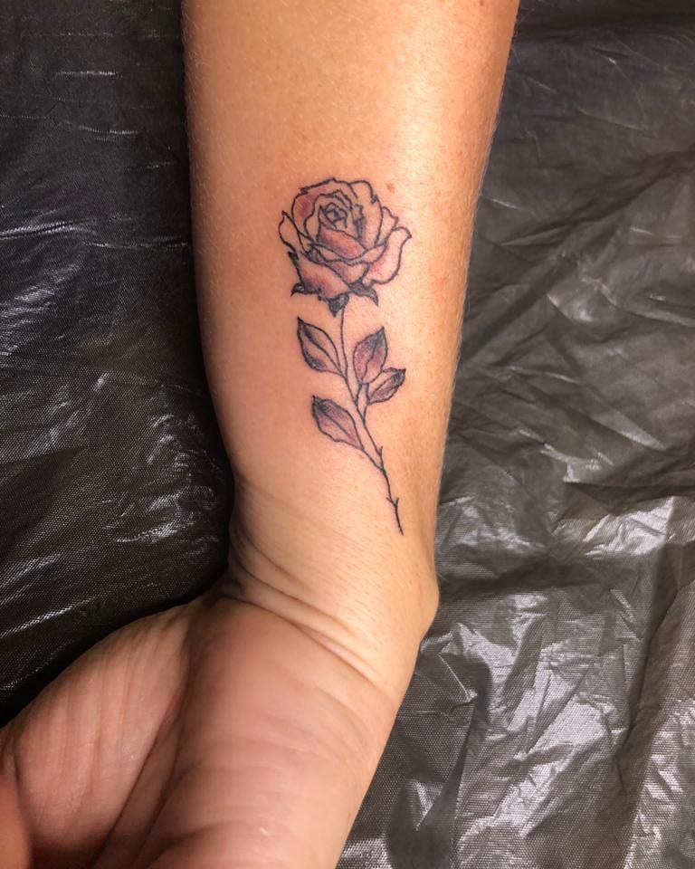A forearm tattoo of a single rose with leaves on a wrist
