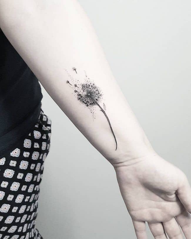 A dandelion tattoo on a forearm, with seeds blowing away