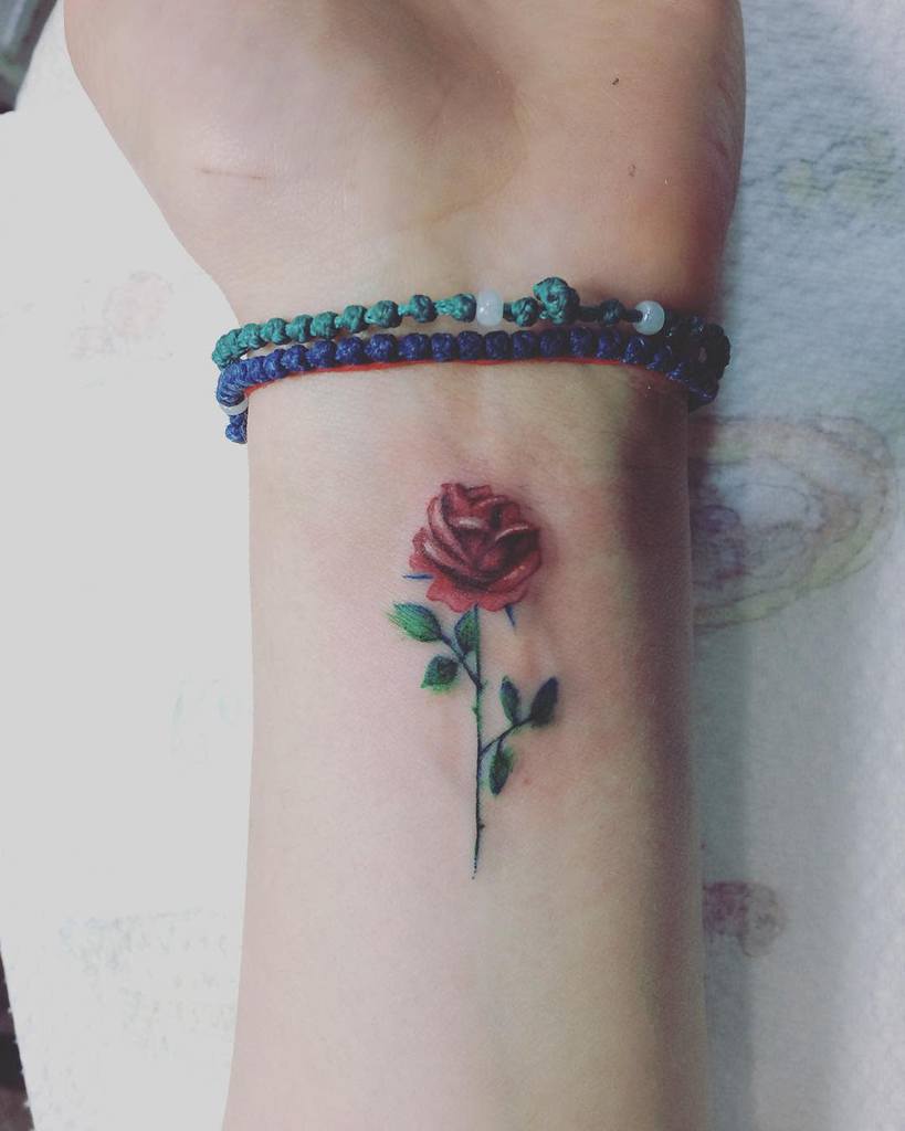 Realistic red rose tattoo on the wrist, featuring fine details and green leaves