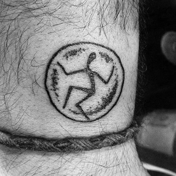 Black and white tattoo of a stylized figure within a circular design, evoking movement and energy through simple, abstract lines and geometric shapes.
