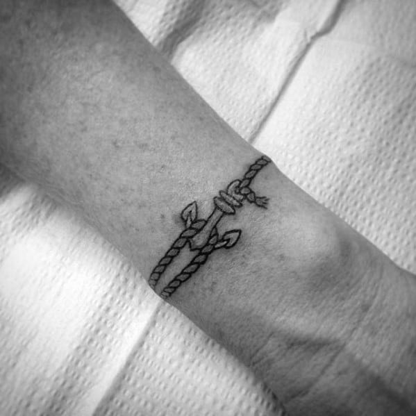 Small and delicate anchor tattoo on the wrist with a wrapped rope, featuring fine black lines, symbolizing stability, strength, and a nautical connection.