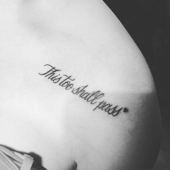 A "This Too Shall Pass" tattoo in cursive with a small heart, on the upper shoulder area.
