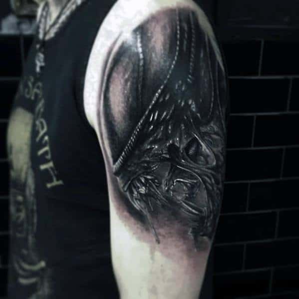 Black and grey Xenomorph tattoo on upper arm with realistic shading, featuring the alien’s elongated head and intricate facial details.