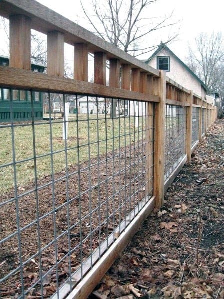 Wooden fence lining a yard, scattered with fallen leaves; houses and bare trees stand in the background