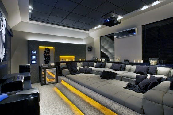 Modern home theater with a large gray sectional sofa, ambient lighting, and a ceiling-mounted projector