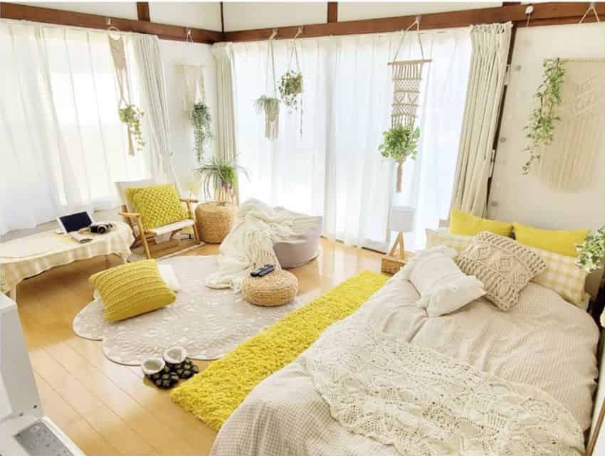 Bright bedroom with stylish yellow decor, cozy bed, plants, and natural light streaming through large windows
