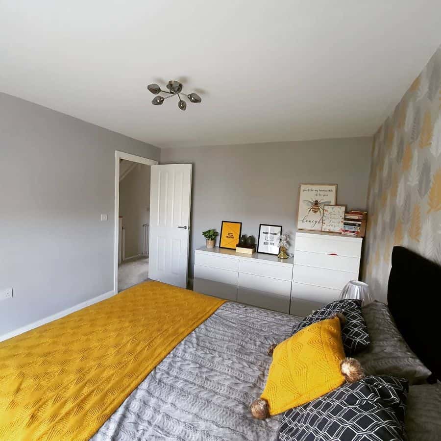 Modern bedroom with gray walls, cozy yellow bedding, white dresser, and decorative accents on top