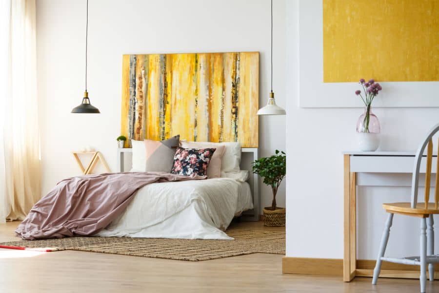 Modern bedroom with a bed, vibrant yellow artwork, colorful pillows, and a desk, creating a bright and airy atmosphere