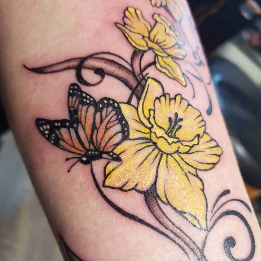 A beautiful tattoo featuring vibrant yellow daffodils intertwined with delicate swirls, accompanied by a colorful butterfly, adding movement and life to the design.