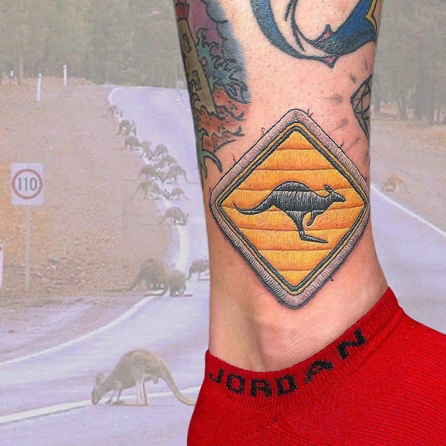 Realistic stitched-effect tattoo of a yellow road sign featuring a kangaroo silhouette, designed to resemble embroidery.