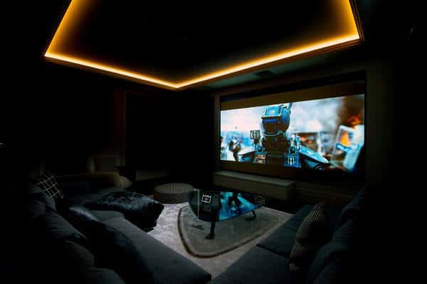Home theater with dim lighting, showing a robot movie on the screen; cozy seating surrounds a central coffee table