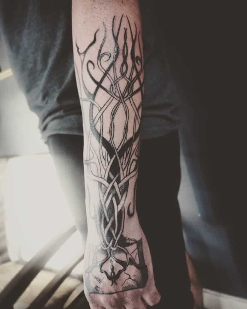 This tattoo features an intricate, abstract tree design with interwoven branches and roots, creating a striking, symbolic look on the forearm.