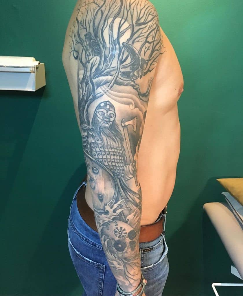 The tattoo sleeve depicts Yggdrasil with intricate branches, a Viking warrior, and Norse mythology elements, creating a powerful, detailed design.