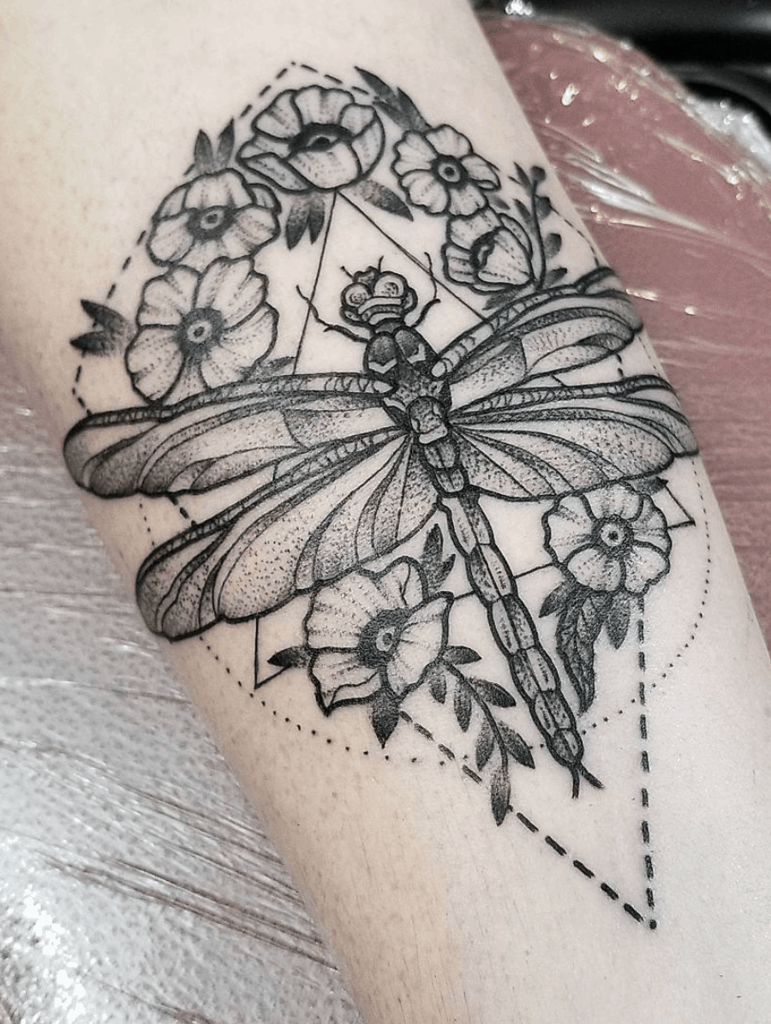 Bold black and grey dragonfly tattoo with floral elements and geometric accents, featuring fine dot work and intricate shading.
