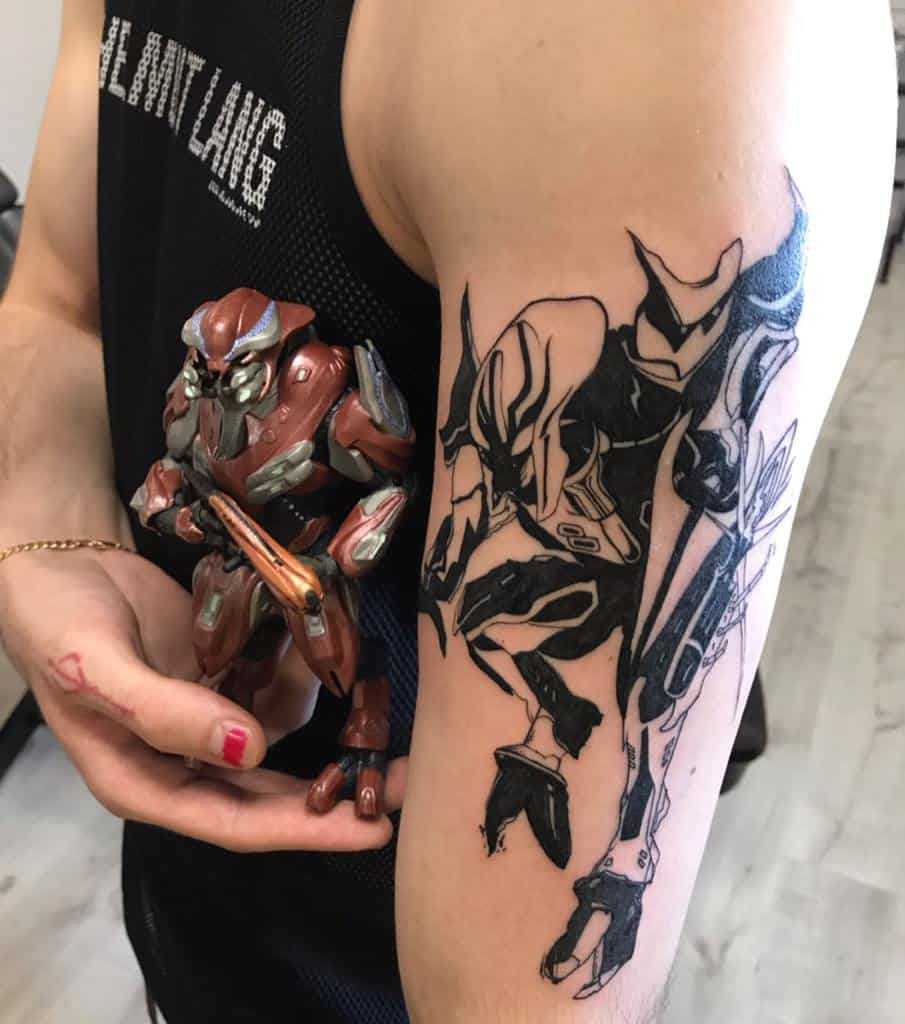 Bold black ink tattoo of a Halo Elite in dynamic combat pose, inked on the upper arm with a stylized design inspired by the game.