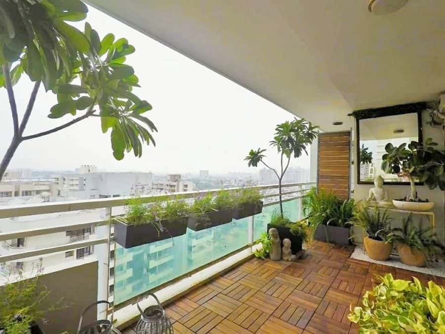 Zen-inspired balcony garden with wooden flooring, potted plants, statues, and city views.