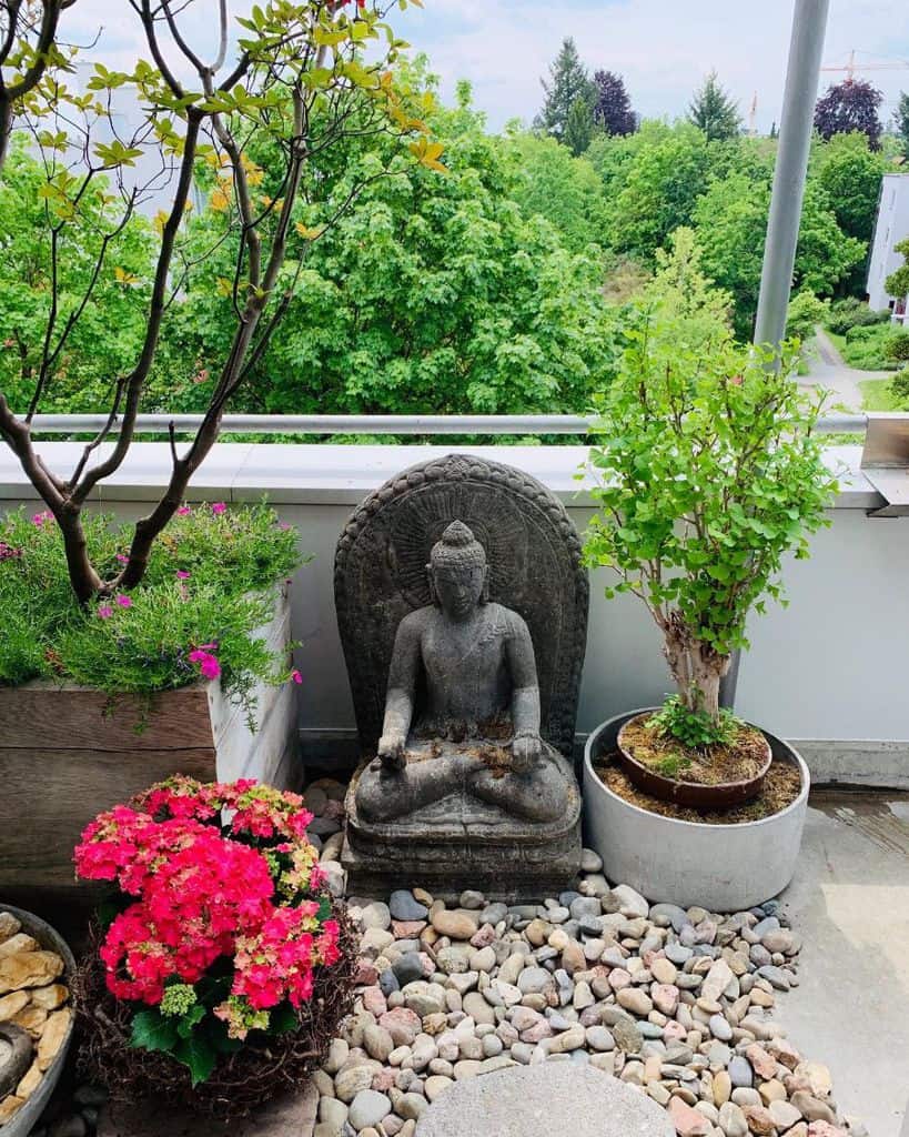 Asian-inspired balcony garden with a Buddha statue, potted plants, and decorative pebbles.