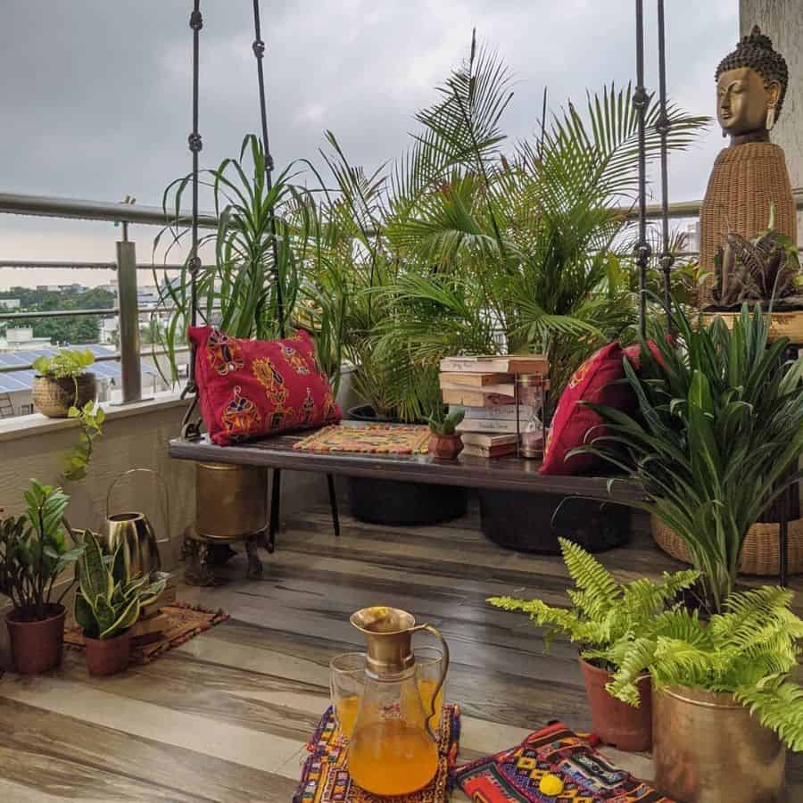 Zen balcony garden with lush plants, a swing, Buddha statue, and vibrant cushions for relaxation.