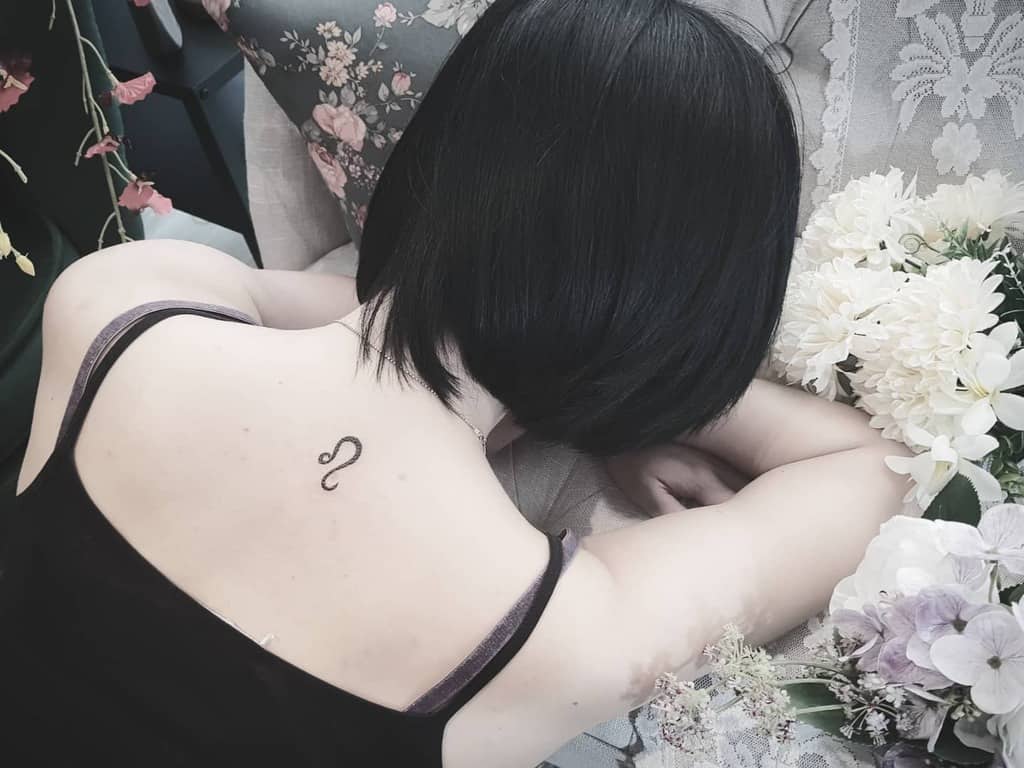 Small black ink Leo symbol tattoo centered on the upper back, blending astrology with a delicate aesthetic.