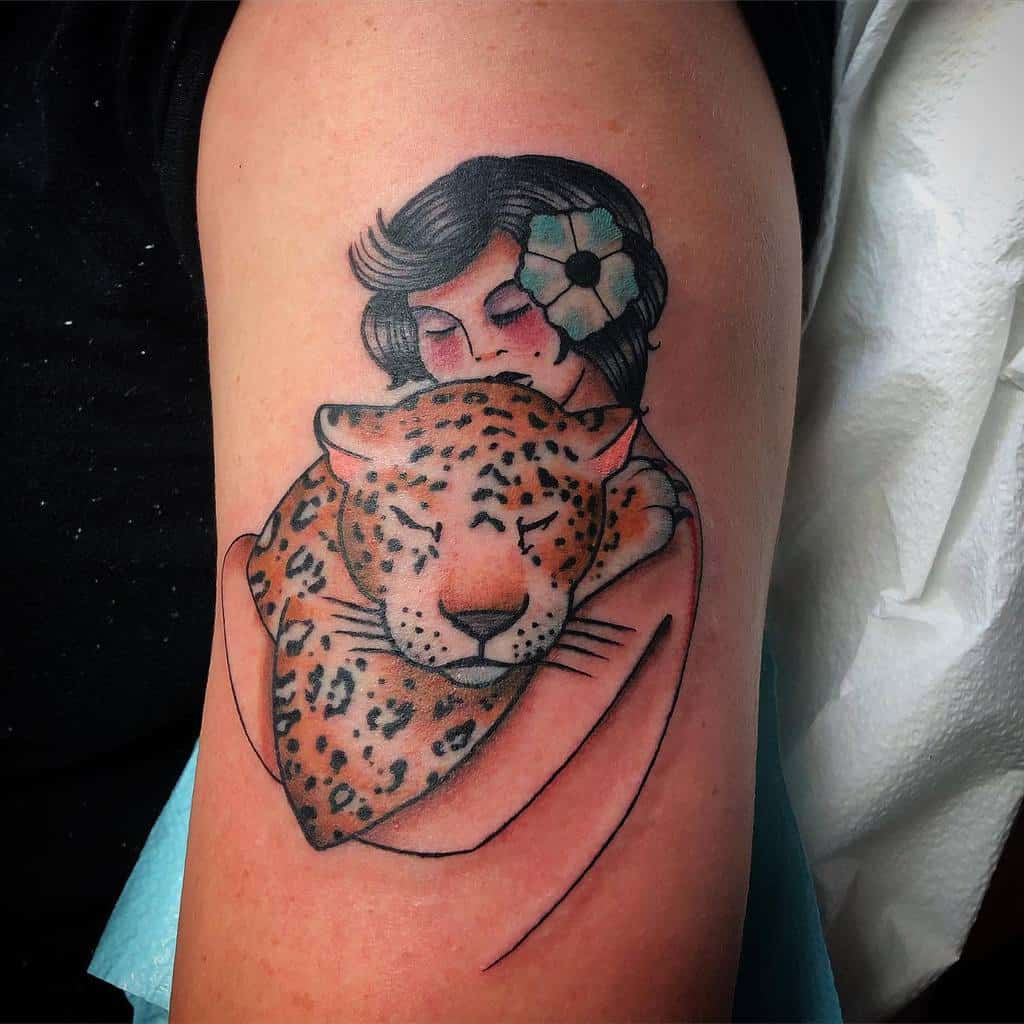 A soft, colorful tattoo of a woman lovingly embracing a leopard, with delicate details like a flower in her hair, creating a peaceful, harmonious design.